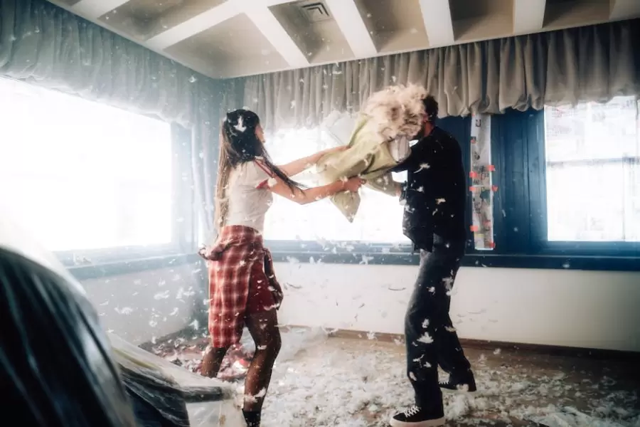 Enérgica pelea de almohadas en interiores entre dos adultos en una habitación luminosa.